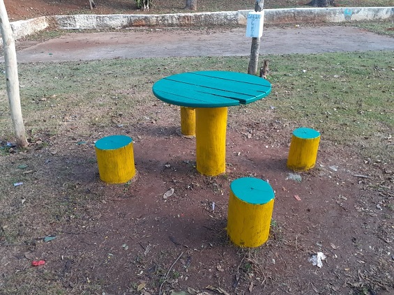 Mesa e banquetas de madeira foram pintadas de azul e amarelo e estão no meio da praça.  